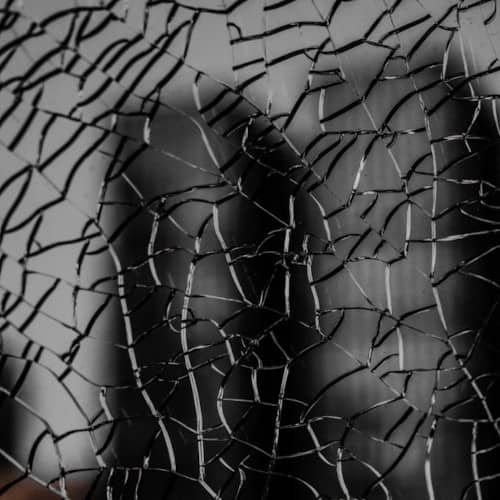 Photo d'une vitre brisée, avec une silhouette humaine derrière