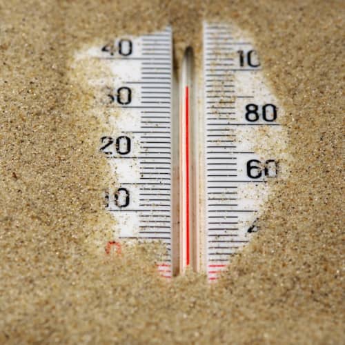 Photo d'un thermomètre à moitié sous le sable, indiquant 35 degrés