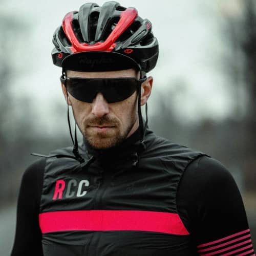 Photo du visage et torse d'un homme en tenue de sport avec lunettes et casque sur une route