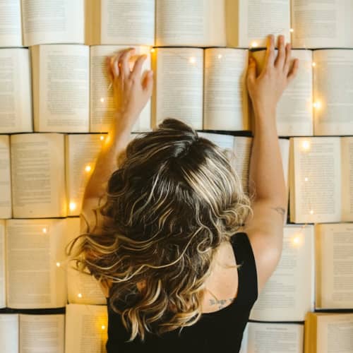 Photo d'une femme allongée, plein de livres ouverts sous elle, illuminés comme magiquement
