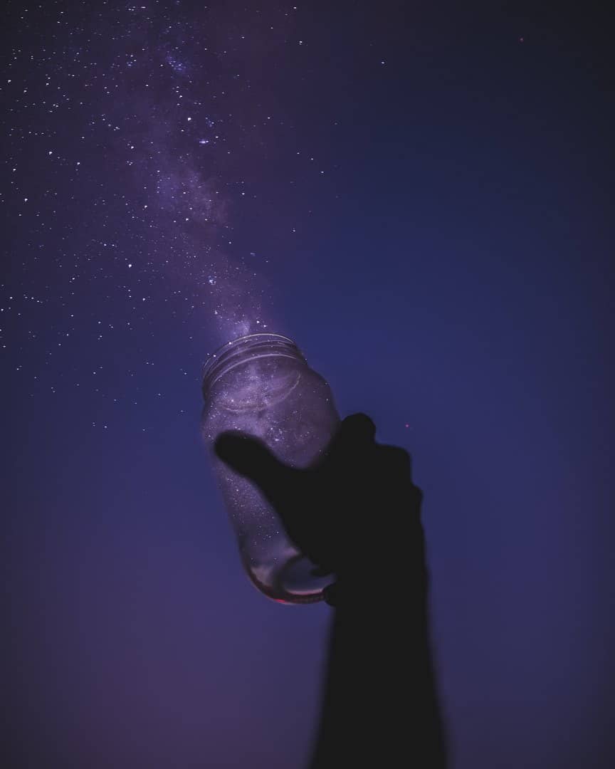 Photo d'un bocal tendu vers le ciel étoilé, comme si les étoiles sortaient du bocal